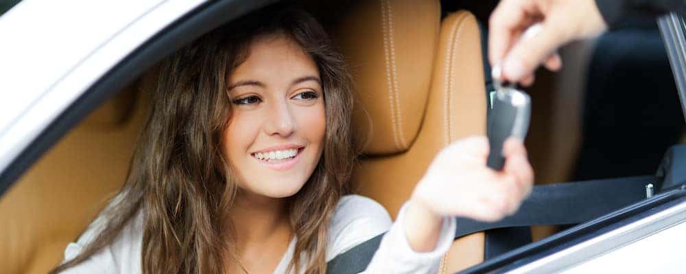 Woman sitting in a car getting the keys dropped into her hand through the window