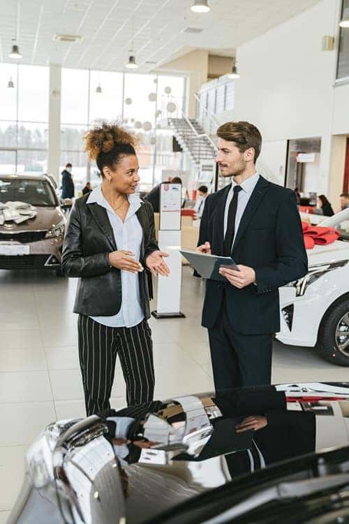 Man in Business Suit Discussing with Woman in Black Blazer around a car