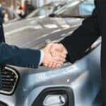 Two people shaking hands in front of a car