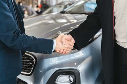 Two people shaking hands in front of a car
