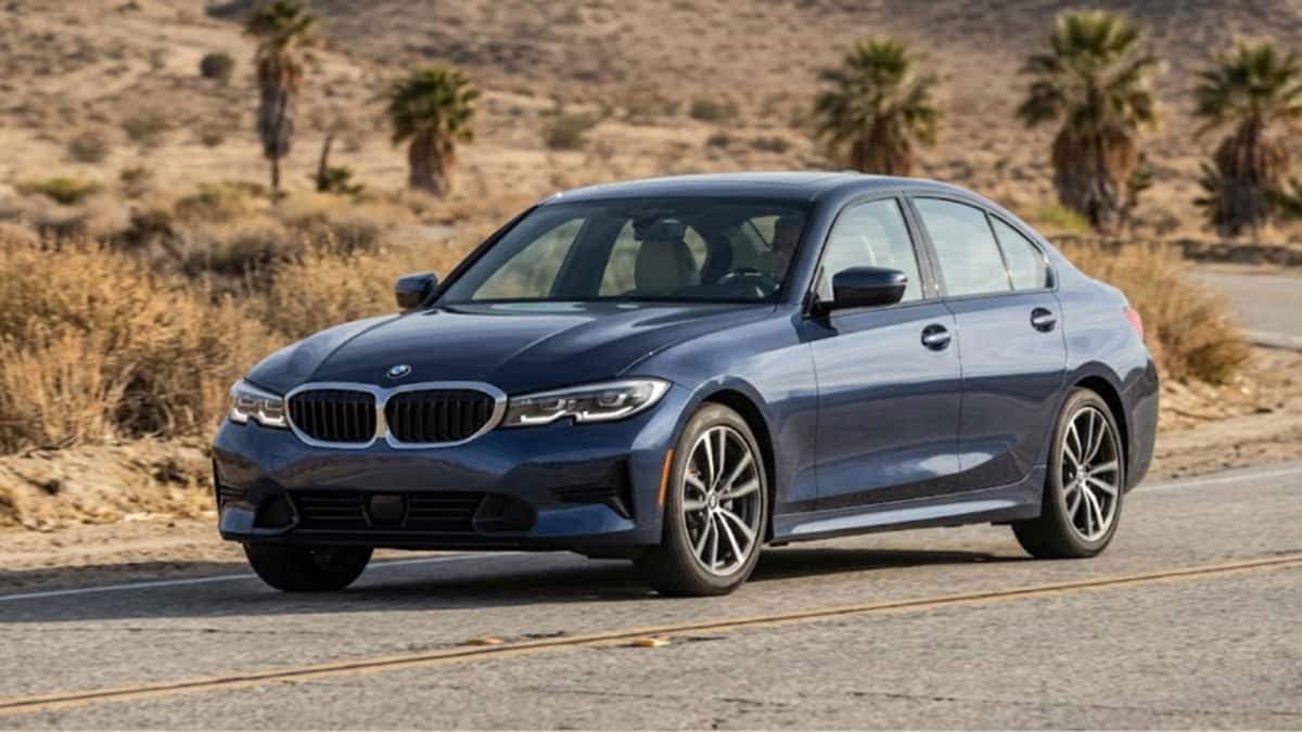Dark blue BMW sedan driving on a desert road lined with palm trees
