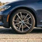 Close view of the front tire and alloy wheel on a dark blue BMW sedan parked on a desert road with palm trees