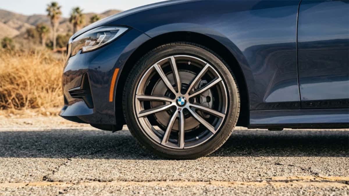 Close view of the front tire and alloy wheel on a dark blue BMW sedan parked on a desert road with palm trees