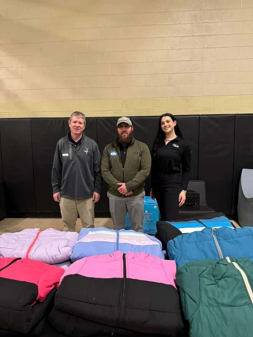 Three team members in front of coats