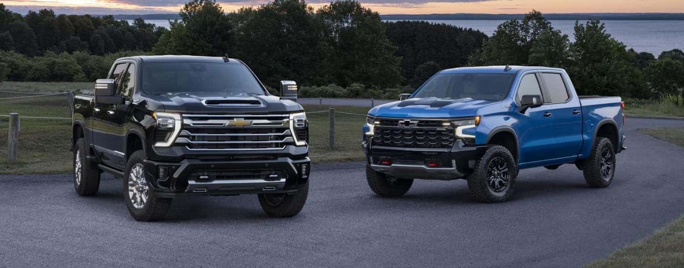 Black 2024 Chevy Silverado 2500 HD High Country and blue 2024 Chevy Silverado 1500 ZR2 on a trail
