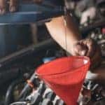 Male adding oil with a funnel after a do-it-yourself oil change.