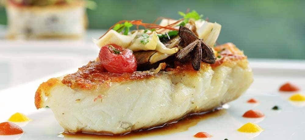 grilled fish on a plate with decorative sauce