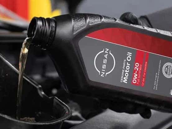A gloved hand pours Nissan Motor oil into a funnel
