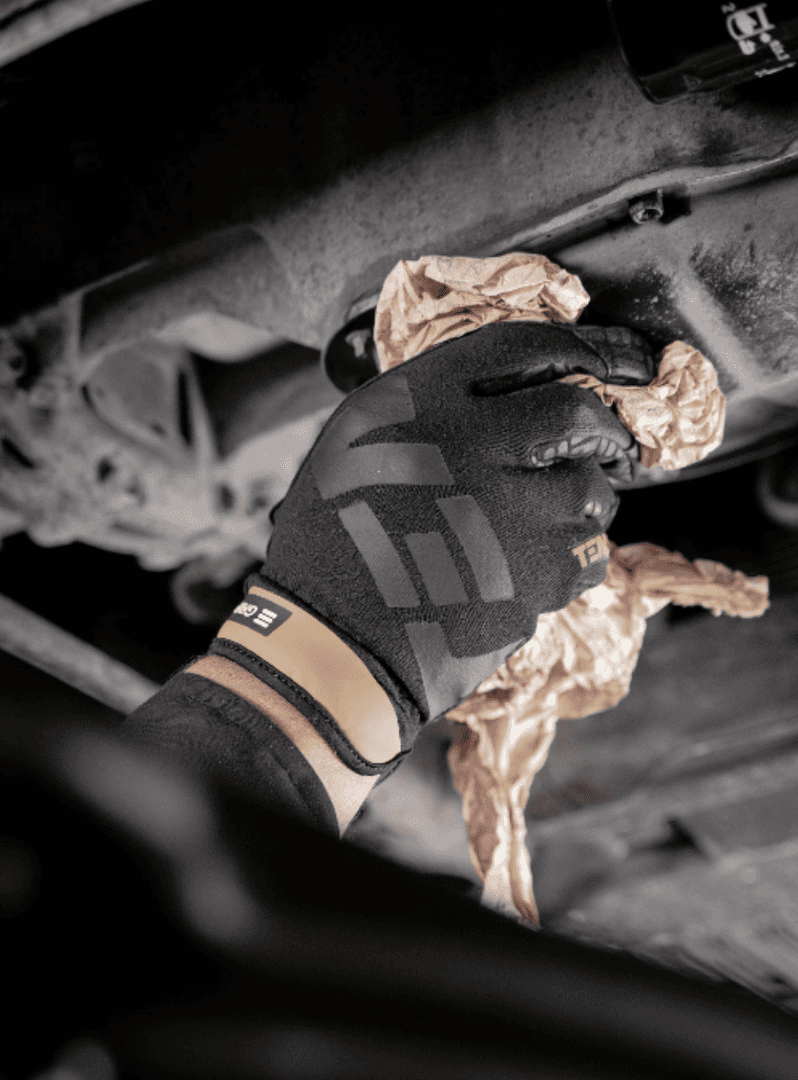 A gloved hand using a rag to twist a bolt on a car
