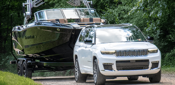 A white 2024 Jeep Grand Cherokee towing a large boat