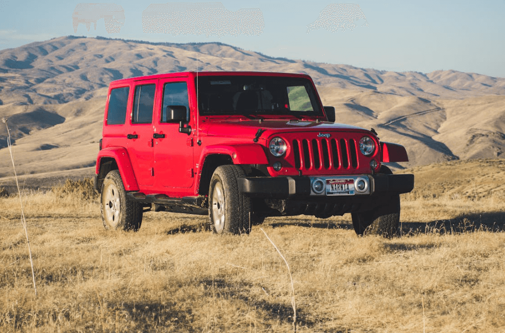 A red Jeep Wrangler parked in grassland with mountains behind