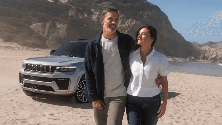 A couple on a beach near a parked 2026 Jeep Grand Cherokee SUV