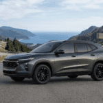 Dark grey Chevrolet Trax LT crossover SUV driving on a winding coastal highway, with mountains and ocean in the background.