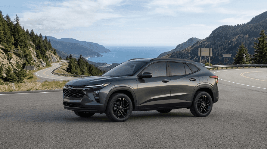 Dark grey Chevrolet Trax LT crossover SUV driving on a winding coastal highway, with mountains and ocean in the background.