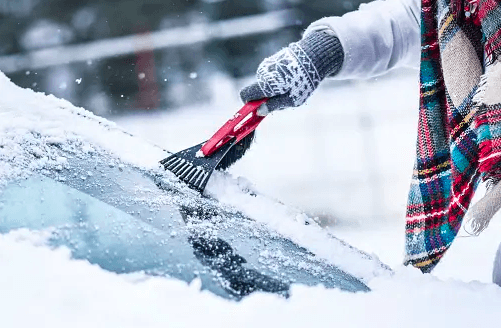 woman cleans snow off car in winter.