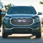 A popular GMC SUV, a dark grey 2021 GMC Terrain Denali, is shown in the park with people jogging past it.