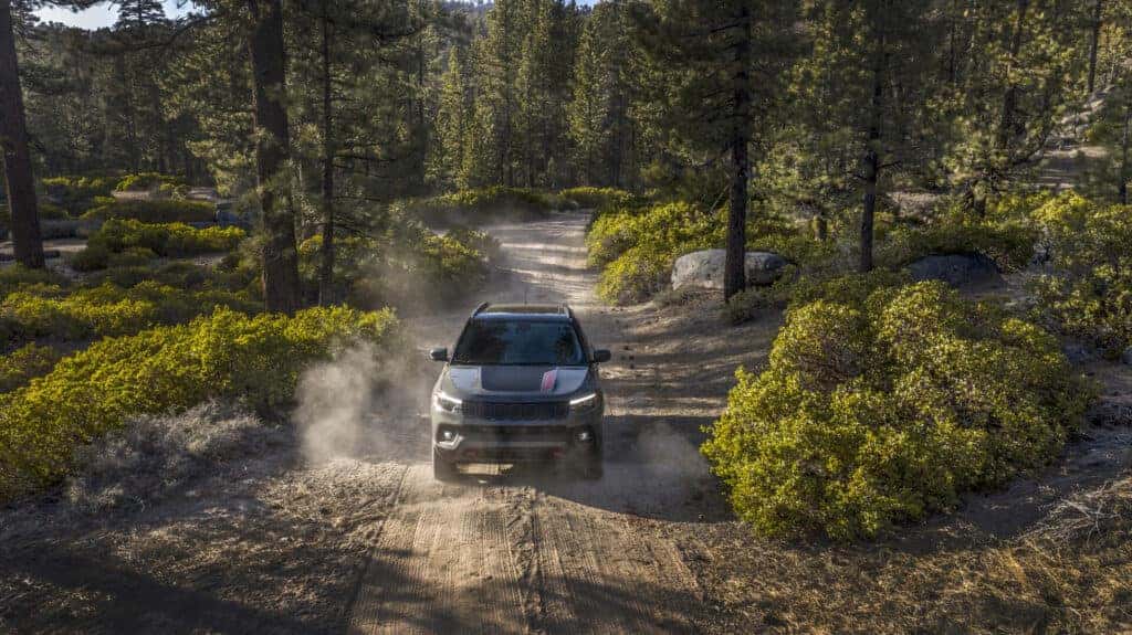2025 Jeep Compass driving off-road through a forest trial.