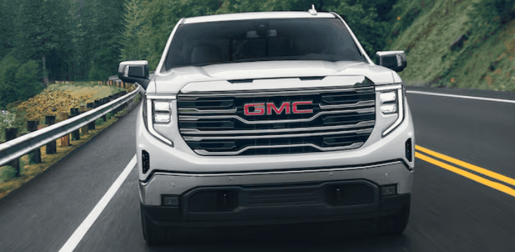 The front grille of a 2024 GMC Sierra 1500 driving on a two-lane mountain highway