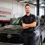 technician leaning against hood of a vehicle, holding a wrench in the service bay