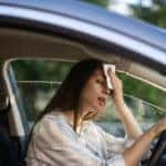 Woman driver being hot during heat wave in car, suffering from hot weather wipes sweat from forehead