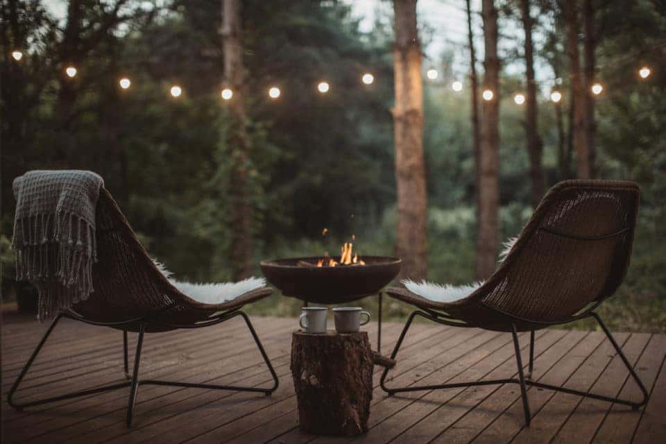 Back porch with two cozy chairs on it and fireplace. Blankets and coffee cups waiting for someone to enjoy in them.