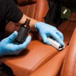 A man applies protective treatment to leather car interior.