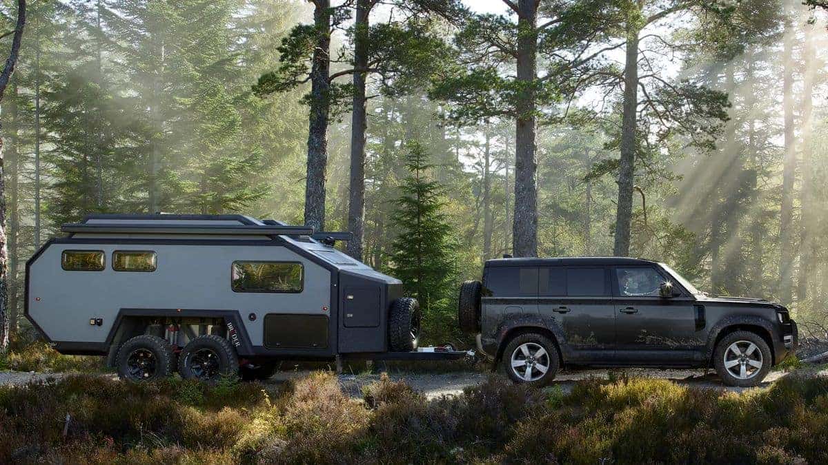 2026 Land Rover Defender towing a trailer through a forest