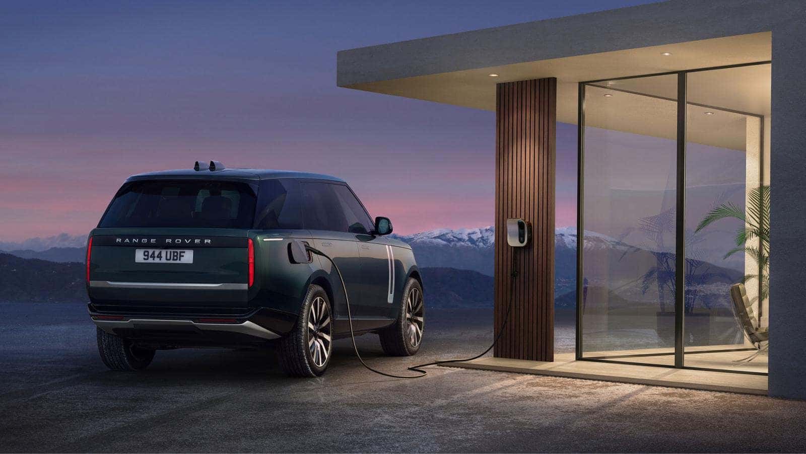 Range Rover Electric in Belgravia Green charging at a home wall box at dusk, rear three-quarter view