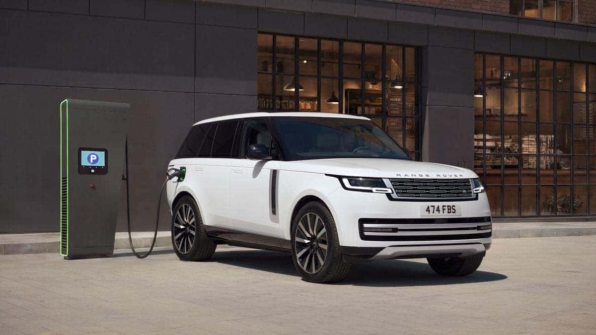 Range Rover Electric in white plugged into a public DC fast charger on a city street, front three-quarter view