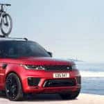 red 2019 range rover sport parked on beach with bicycle mounted on roof