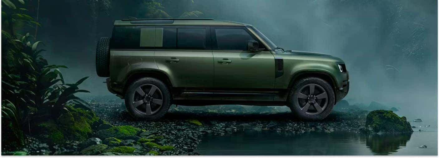 Side profile view of a green 2026 Land Rover Defender 110 SUV in a misty rainforest setting.