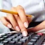 Photo of hands holding pencil and pressing calculator buttons over documents