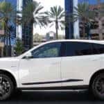 Side view of white RDX parked in front of palm trees