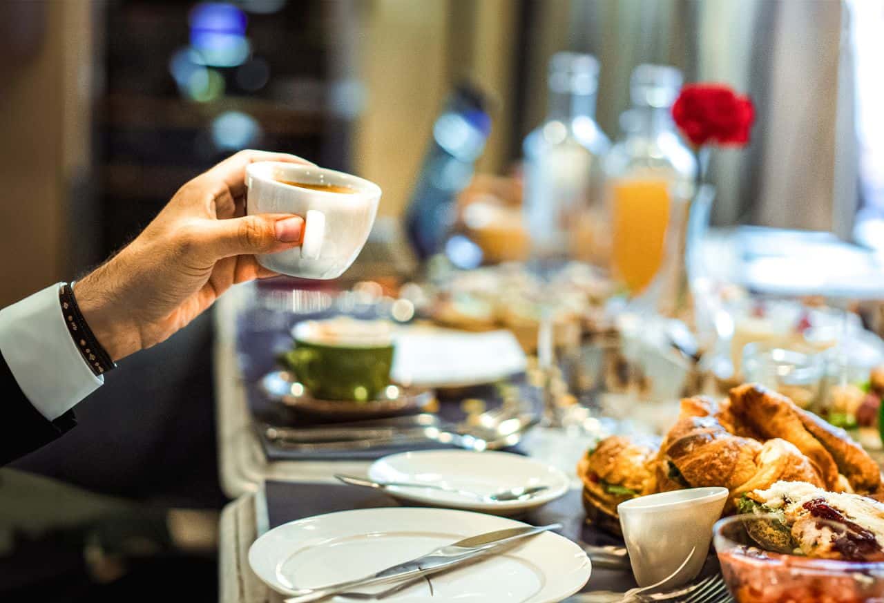 Person holding a cup of espresso over a dinner table