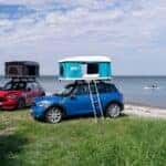 Two used MINI vehicles parked by a coast with campers on their roofs