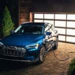 A blue Audi e-Tron charging in a driveway.