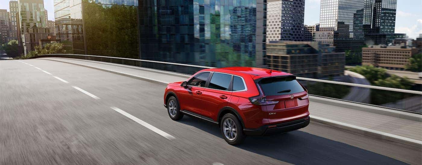 A red 2023 Honda CR-V EX is shown from a rear angle driving on a highway.
