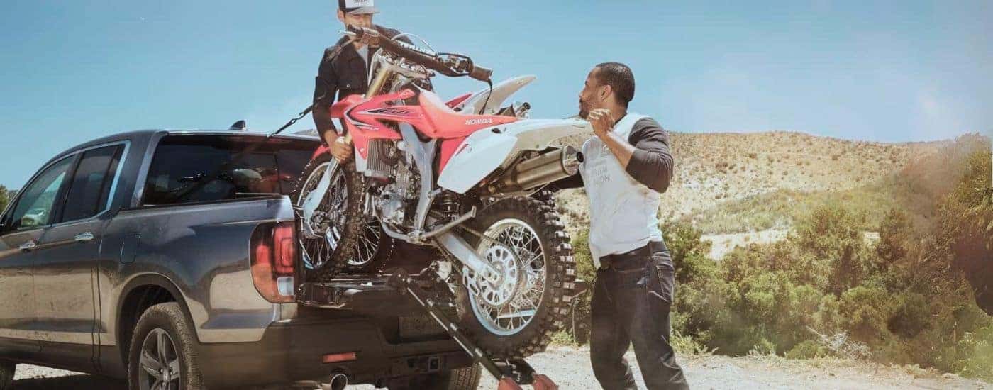 People are shown loading a dirt bike into the bed of a grey 2022 Honda Ridgeline RTL-E.