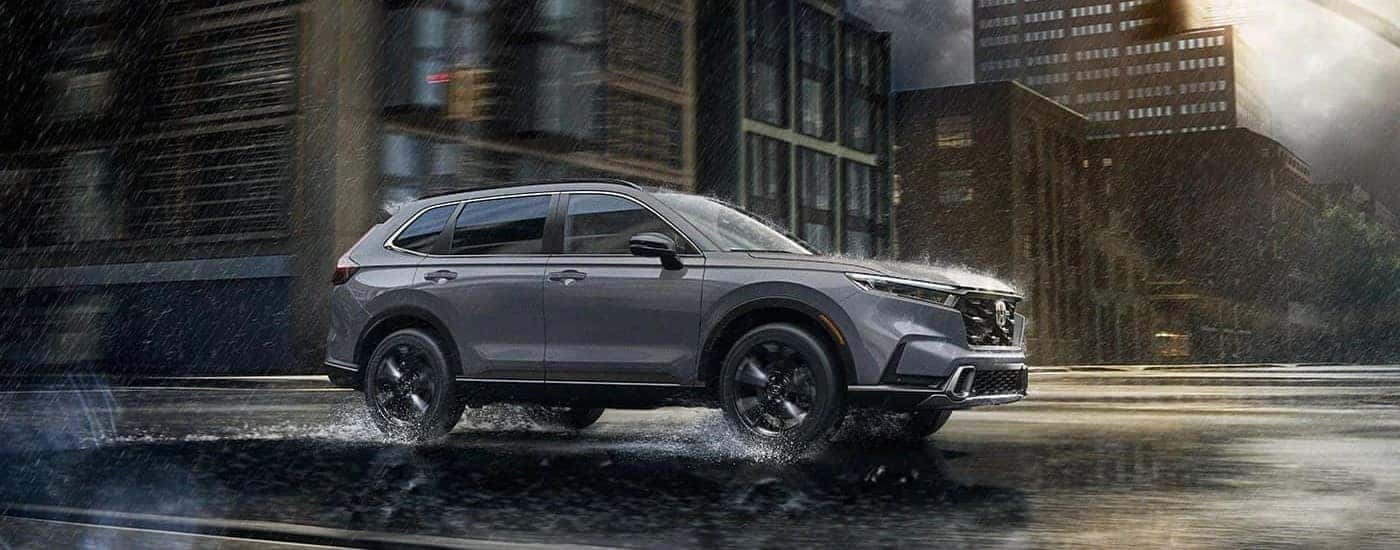 A grey 2023 Honda CR-V Sport Touring Hybrid driving through a rainy city.