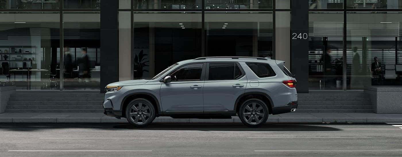 Side angle view of a grey 2023 Honda Pilot Sport parked beside a curb.
