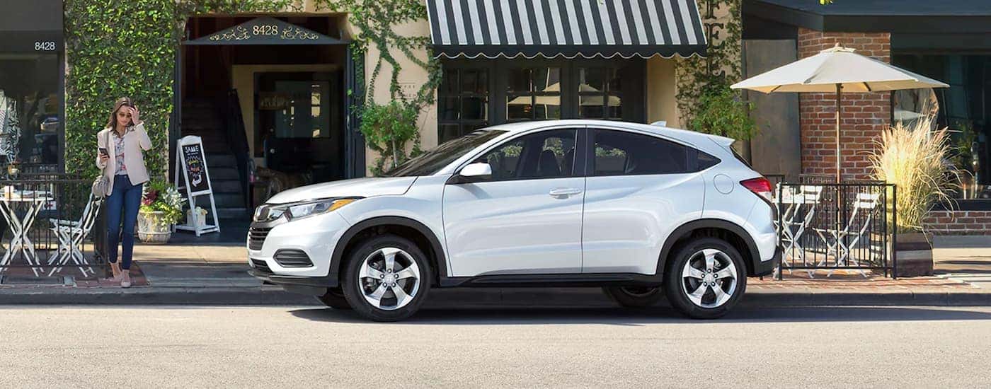 Side angle view of a white 2020 Honda HR-V LX parked by a city curb.