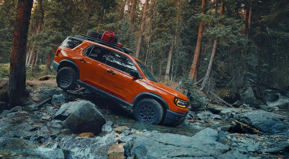 An orange 2025 Honda Passport Trailsport Elite driving through a river.
