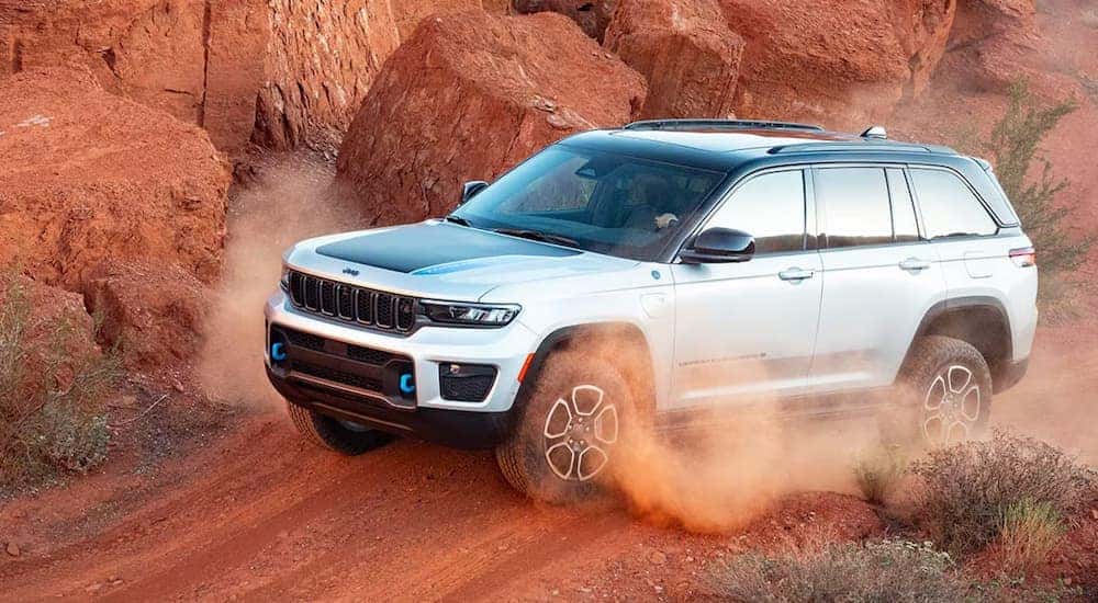 A silver 2025 Jeep Grand Cherokee 4xe Trailhawk off-roading on a dusty path.