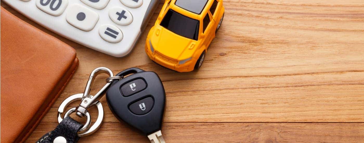 A set of car keys near a yellow toy car on a table.