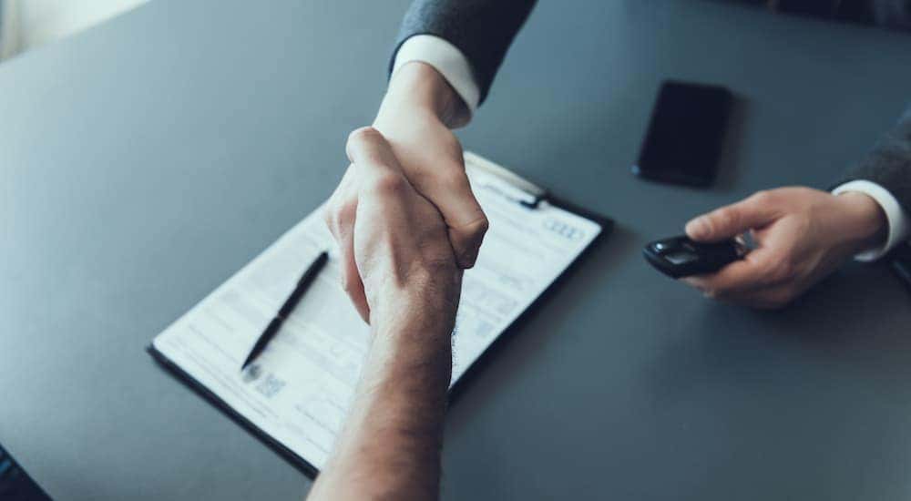A handshake is shown over paperwork after a customer searched how to "sell my car".