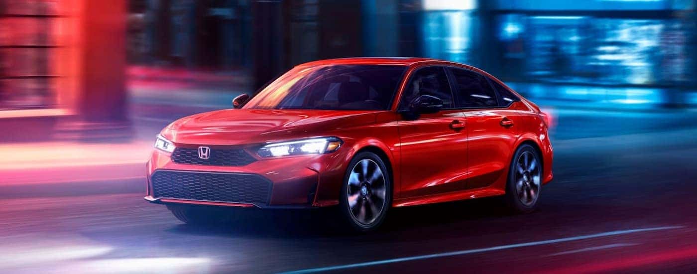 A red 2025 Honda Civic driving down a city street at night