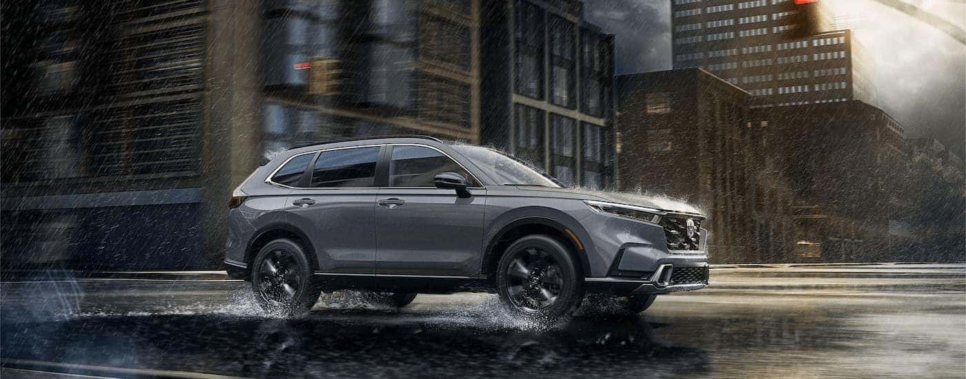 Grey 2024 Honda CR-V Hybrid driving through a city in the rain