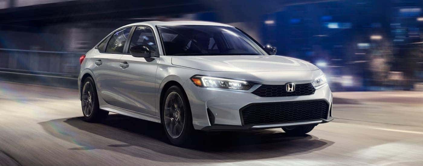 Silver 2025 Honda Civic Sport Hybrid driving on a city street at night