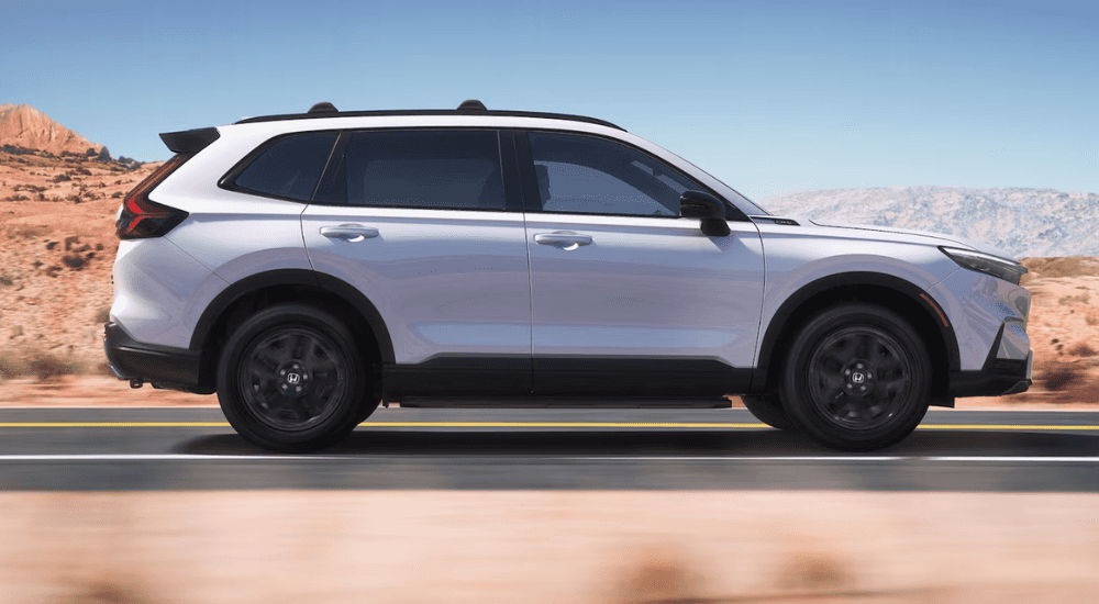White 2026 Honda CR-V Hybrid Sport Touring driving down the road