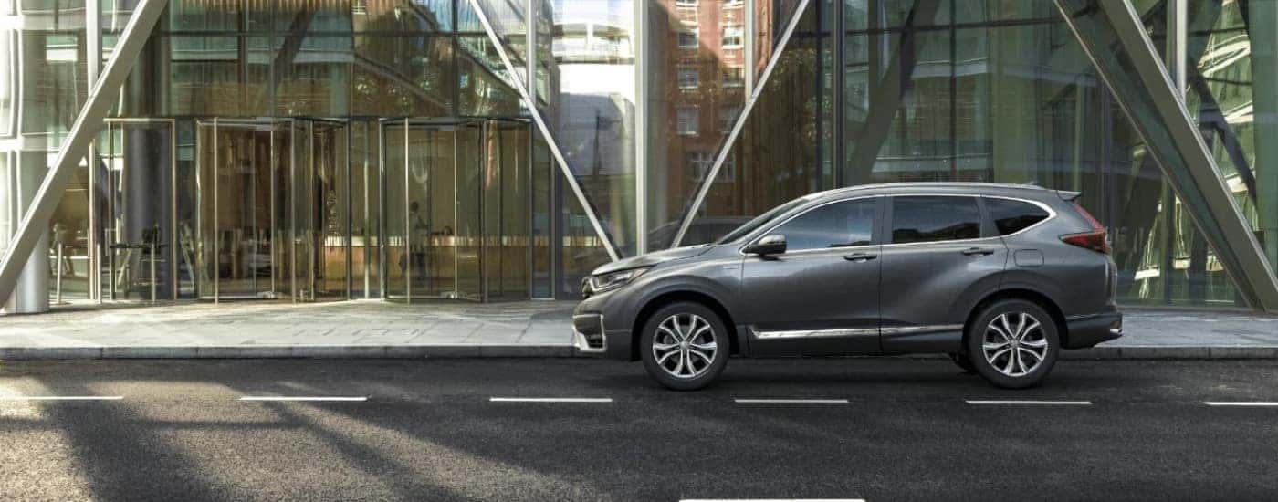Gray 2022 Honda CR-V Touring Hybrid driving next to a building.